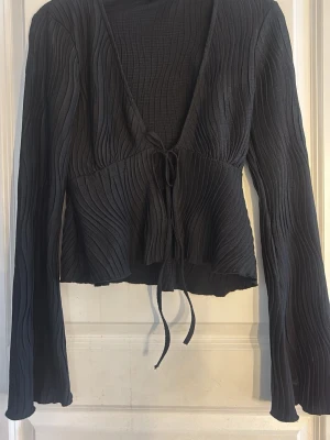 Svart omlottopp från Gina Tricot - Säljer en svart omlottopp från Gina Tricot i storlek S. Toppen har långa ärmar, v-ringning och knyt framtill. Materialet är ribbat och ger en snygg struktur. Perfekt till jeans eller kjol för en trendig look.