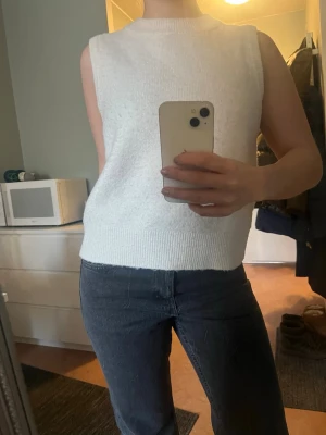 Beige ärmlös stickad tröja Mango MNG - Säljer en beige/vit ärmlös stickad tröja från Mango MNG i ullblandning. Tröjan har ribbad rund halsringning och breda muddar nedtill. Typ en väst! Passar xs/s/m. 