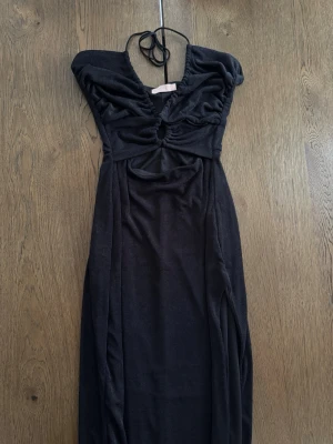 Svart långklänning med slits - Svart långklänning från Nelly med tunna halterneckband, cut out framtill och hög slits på sidan. Storlek S, använd 1 gång.