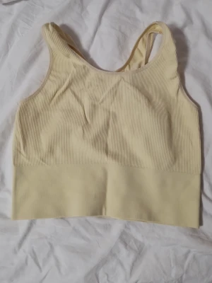 Ljusgul ribbad linnetopp - Säljer en ljusgul ribbad linnetopp med bred resår nedtill. Toppen är ärmlös och en sport linne
