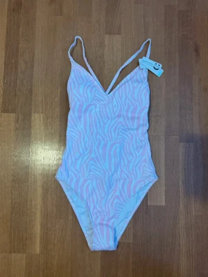 baddräkt i pastell - storlek M - ny med prislapp - Säljer en superfin baddräkt från Cubus i ljusrosa och vitt med zebramönster. Modellen har smala axelband som korsas i ryggen och snygga cut-outs med knyt baktill. Perfekt för strandhäng eller poolparty!