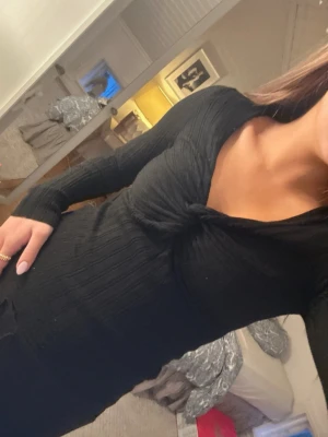 Svart ribbad långärmad topp - Säljer en svart långärmad topp med ribbad struktur och snygg twistad detalj framtill vid bysten. Toppen har v-ringad hals och sitter tight mot kroppen, perfekt att styla med jeans eller kjol. Materialet är mjukt och stretchigt, vilket gör den superbekväm.