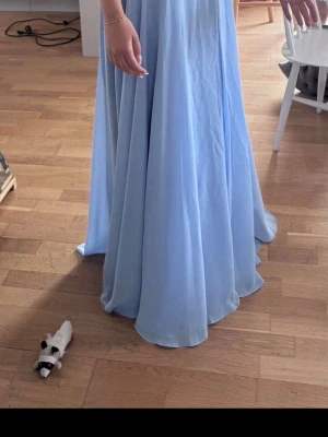 Ljusblå balklänning  med spets och slits  - Säljer en ljusblå balklänning från JJ's House med v-ringning och spetsdetaljer upptill. Klänningen har öppen rygg med snörning, så enkelt att ha den hur tight man vill. Klänningen har även en slits. Bara använd en gång på självaste studentbalen så klänningen är i väldigt bra skick. Nypris:1842