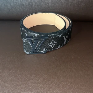 Svart bälte - Snyggt svart bälte med klassiskt monogrammönster och spänne i svart. Bältet är gjort i skinn och har en lyxig känsla med kontrasterande ljus insida. Perfekt accessoar för att lyfta din outfit.