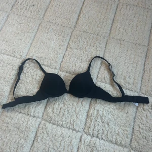 Bh 70B - En stilren svart Bh med vadderade kupor och justerbara axelband. Tillverkad i mjukt och stretchigt material för en bekväm passform, push-up.