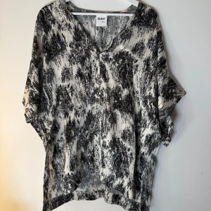 Svartvit blus från DAY Birger et Mikkelsen - Säljer en luftig svartvit blus från DAY Birger et Mikkelsen. Blusen har ett abstrakt mönster, v-ringning och vida korta ärmar. Perfekt för dig som gillar en avslappnad men ändå stilren look. Materialet känns lätt och svalt mot huden. Storlek 40/L