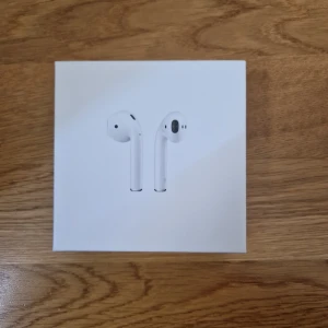 AirPods 2 - Snygga och populära Apple AirPods 2 i originalförpackning. Trådlösa hörlurar med laddningsetui, perfekt för musik och samtal. Produkten ser ut att vara i nyskick utan synligt slitage eller defekter. Enkel anslutning till iPhone och andra Apple-enheter.