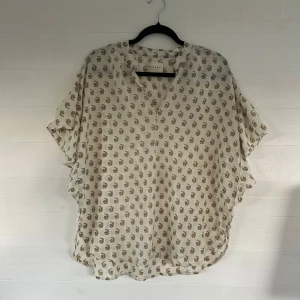 Blommig blus från Sissel Edelbo - Luftig blus från Sissel Edelbo i ljusbeige med små blommiga mönster i grönt och orange. Blusen har v-ringning, korta vida ärmar med volang och en avslappnad passform. Perfekt för en chill och trendig look.🤩💕