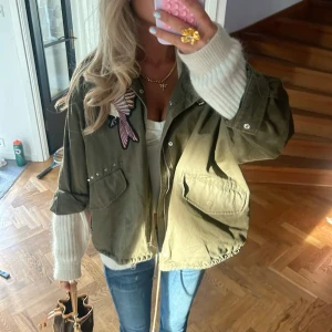 Olivgrön overshirt med broderier - Olivgrön overshirt med coola broderier av orm, fågel och blommor. Jackan har dragkedja framtill, stora fickor och snörning i nederkant. Oversized passform och långa ärmar. Perfekt för lager-på-lager och streetstyle.