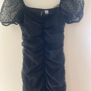 Svart prickig kortklänning Divided - Supersnygg svart kortklänning från Divided (HM) med puffiga kortärmar i mesh och prickigt mönster. Klänningen har rynkade detaljer framtill.❣️