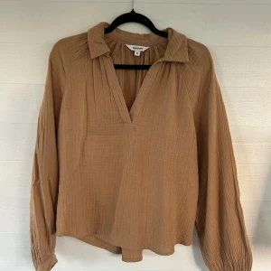 Beige/brun blus - Säljer en beige/brun blus från Kappahl i storlek XS. Blusen har v-ringning, krage och långa ärmar med lätt rynkade muddar. Tillverkad i ett mjukt, strukturerat bomullstyg som ger en avslappnad och trendig look.🤩💕