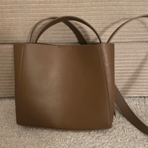 Brun axelväska från Gina Tricot - Gina tricot pu midi bag. Snygg brun axelväska i stilren boxig modell från Gina Tricot. Väskan har både handtag och lång axelrem. 