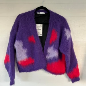 Lila fluffig fodrad kofta från Zara - Supermjuk och fluffig lila kofta från Zara med coola röda och ljuslila mönster. Koftan har en loose passform, lång ärm och är stickad i ett riktigt mysigt material. Perfekt för dig som vill sticka ut med färg och stil!
