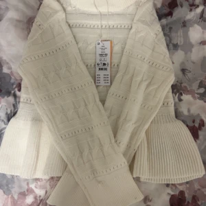 Vit stickad tröja med mönster - Säljer en vit stickad tröja från Gina med snyggt kabelmönster och breda ribbade muddar vid ärmslut. Tröjan har lång ärm och hög krage som ger extra mysfaktor. Perfekt för dig som gillar stilrena och bekväma plagg.