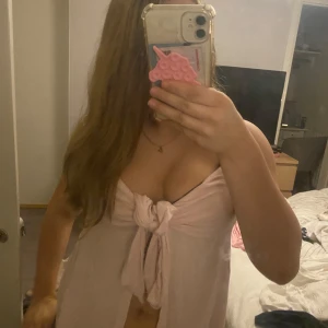 Ljusrosa omlott tubtopp med knyt - Säljer en ljusrosa tubtopp med omlott och knyt framtill. Toppen är ärmlös och har en luftig, flowy passform som ger en avslappnad och trendig look. Perfekt för varma dagar eller sommarens alla tillfällen.