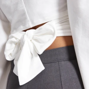 Långärmad topp lager157 - Ny med prislapp, Säljer en vit croppad topp med långa ärmar och en snygg knytrosett i ryggen. Toppen har rund halsringning och är figurnära framtill, vilket ger en fräsch och trendig look. Perfekt att styla med höga byxor för en cool outfit.