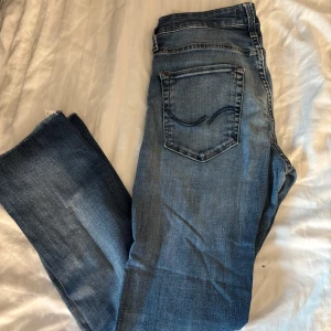 Blå jeans från Jack & Jones - Snygga blå jeans från Jack & Jones med klassisk femficksdesign och slitningar för en cool look. Jeansen har normal passform och raka ben, tillverkade i mjukt bomullsmaterial med lite stretch för extra komfort.