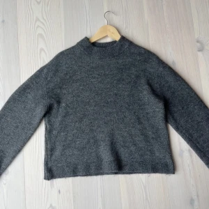 Mörkgrå stickad tröja från Gina Tricot - Mysig mörkgrå stickad tröja från Gina Tricot med högre ribbad halsringning och raka ärmar. Perfekt för lager-på-lager och enkel att matcha med jeans eller kjol. Klassisk modell med ribbade muddar vid ärmslut och nederkant.💕