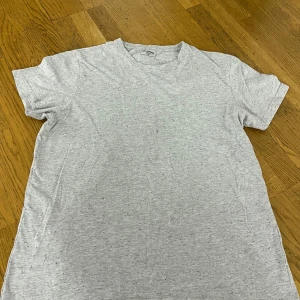 Gråmelerad t-shirt från Dressmann XL - Enkel och stilren gråmelerad t-shirt från Dressmann i storlek XL. T-shirten har korta ärmar, rund halsringning och är tillverkad i mjuk bomull. Perfekt för en chill och avslappnad look.