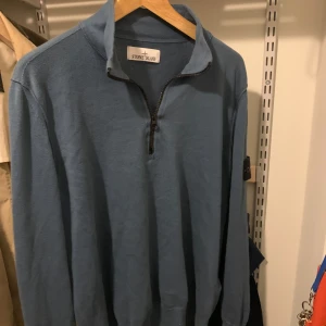 Blå Stone Island half zip tröja - Säljer en blå långärmad tröja från Stone Island med klassisk patch på ärmen. Tröjan har en hög krage och half zip-dragkedja framtill. Materialet är mjukt och stickat, perfekt för lager-på-lager under hösten eller vintern. Dragkedjan är lite trasig längst ner men den funkar fortfarande.