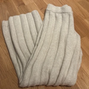 Ribbade stickade byxor i ljusbeige - Mysiga ribbade stickade byxor i ljusbeige färg. Byxorna är lågmidjade och är tillverkade i ett mjukt, värmande bomulls material som passar perfekt för chill dagar. Snyggt ribbat mönster ger en trendig look.