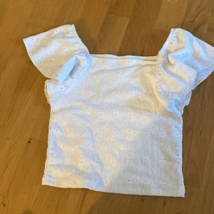 Vit blus med broderade detaljer Kappahl - Söt vit blus från Kappahl i storlek 158/164. Toppen har korta, voluminösa ärmar och är dekorerad med broderade hålmönster över hela tyget. Perfekt för en fräsch och somrig look.
