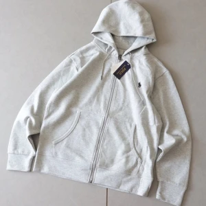 Grå hoodie från P - Snygg ljusgrå hoodie från P med dragkedja framtill, huva med snörning och två stora fickor. Klassisk broderad logga på bröstet. Perfekt för en chill och avslappnad stil.