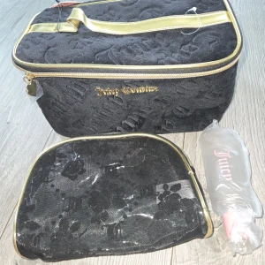 Juicy Couture svart necessärset - Snyggt necessärset från Juicy Couture i svart frotté med guldiga detaljer och dragkedja. Stora väskan har präglad logga och handtag i guld, insidan är ljusrosa. Mindre väska i svart mesh med blommönster och guldiga kanter. Perfekt för smink eller resor.