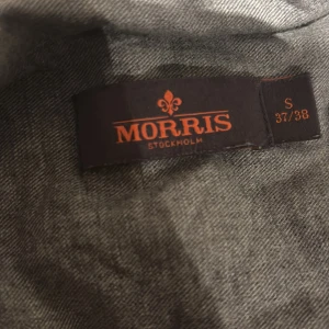 Grå skjorta från Morris Stockholm - Snygg grå skjorta från Morris Stockholm i storlek S (37/38). Skjortan har klassisk passform, vita knappar och en broderad logga på bröstet. Perfekt för dig som gillar stilrena och enkla plagg med diskreta detaljer. Knappt använd i perfekt skick ( ny pris 1300kr )