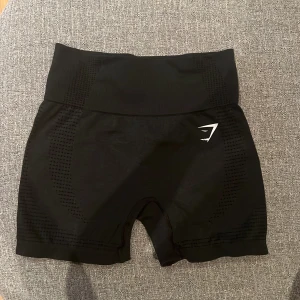 Svarta seamless shorts från Gymshark - Svarta seamless shorts från Gymshark med hög midja och diskret mönstrad struktur i tyget. Stretchigt material som sitter tight och bekvämt, perfekt för träning. Gymshark-logga i vitt framtill. Snygg och sportig look.