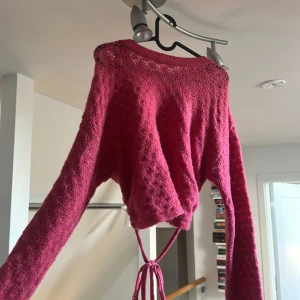 Rosa stickad croppad tröja från Zara - Säljer en rosa stickad tröja från Zara med croppad passform och snygg knytning i midjan. Tröjan har lång ärm och ett diskret hålmönster upptill som ger en cool touch. Perfekt för lager på lager under höst och vinter.