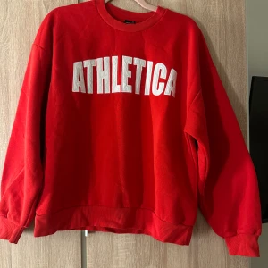 Röd sweatshirt ATHLETICA Gina Tricot - Röd sweatshirt från Gina Tricot med vit ATHLETICA-text framtill. Klassisk rund halsringning, ribbade muddar och avslappnad passform. Perfekt för en sportig look och enkel att styla till jeans eller leggings. Tröjan är sååå skön!