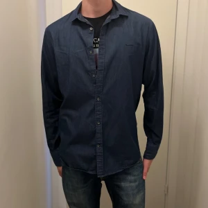 Mörkblå skjorta från Bondelid - Snygg mörkblå skjorta från Bondelid i bomull med skräddad passform. Klassisk krage, knäppning framtill och långa ärmar. Perfekt för dig som gillar stilrena och enkla plagg med en modern touch.