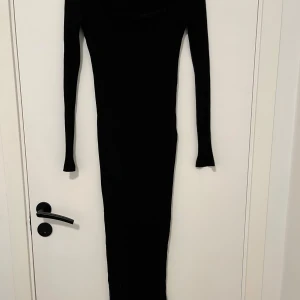 Svart ribbad långklänning - Säljer en svart långklänning med ribbad struktur och lång ärm. Klänningen har en snygg, fyrkantig urringning och sitter tight mot kroppen. Perfekt för dig som gillar minimalistisk och stilren look.