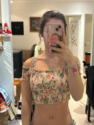 Blommig croppad topp från H&M Divided - Säljer en söt croppad topp från H&M Divided i storlek XS. Toppen är ljusbeige med blommigt mönster i grönt, rosa och orange, off shoulder