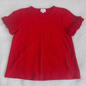 Röd glittrig topp från KappAhl storl 146/152 XS - Säljer en röd glittrig topp från KappAhl med korta ärmar och volangdetaljer. Materialet är mjuk polyester med skimrande effekt som syns tydligt i ljuset. Perfekt för dig som vill sticka ut med färg och glitter. Rund halsringning och loose passform.( barn storlek) Från rök och djurfritt hem.