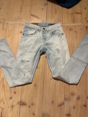 Ljusblå/vit slitna jeans från dondup - Säljer ett par ljusblå jeans från dondup med skinny passform. Jeansen har slitna detaljer och lagningar framtill, klassiska fem fickor och unika broderier på bakfickan. Perfekta för dig som gillar en avslappnad och trendig look.
