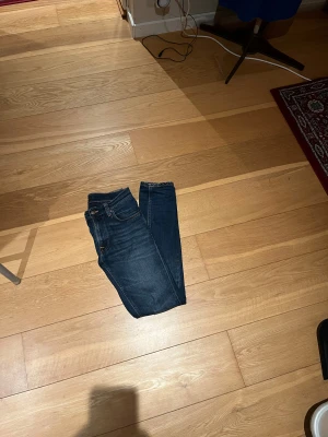 Mörkblå skinny jeans från Nudie - Snygga mörkblå jeans från Nudie med klassisk femficksdesign och smal passform. Jeansen har orangea sömmar och subtila slitningar på låren för en cool look. Tillverkade i stretchig denim som sitter tajt men bekvämt.