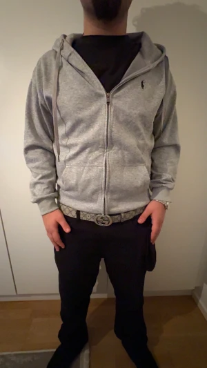 Grå hoodie från Polo Ralph Lauren L - Snygg grå hoodie från Polo Ralph Lauren i storlek 2XL. MEN passar som Xl/L Tröjan har dragkedja framtill, huva med snörning och klassisk Polo-logga broderad på bröstet. Tillverkad i mjuk bomullsmix, perfekt för chill dagar. Långärmad och med praktiska fickor framtill.