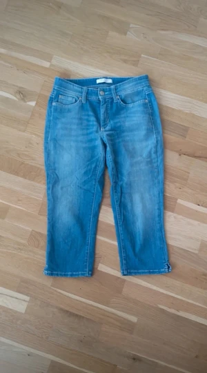 Cambio capri jeans - Ljusblå croppade jeans från Cambio Jeans Vintage Edition. Klassisk femficksmodell med knapp och dragkedja framtill. Jeansen har raka ben och är tillverkade i mjukt denimtyg.