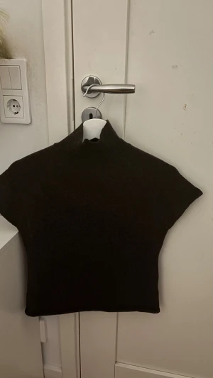 Brun stickad polotopp - Säljer en brun stickad polotopp med korta ärmar och hög krage. Toppen har en clean och enkel design som är lätt att matcha med olika stilar. Perfekt för dig som gillar minimalistiska plagg med lite edge. Vet inte riktigt vart den är ifrån 