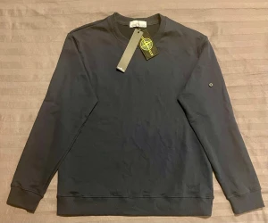  sweatshirt - Stone Island - Svart långärmad sweatshirt från Stone Island i mjuk bomull. Klassisk rund hals och ribbade muddar vid ärmslut och nederkant. Diskret logga på ärmen och taggar kvar. Perfekt för dig som gillar stilrena och snygga streetwear-plagg.