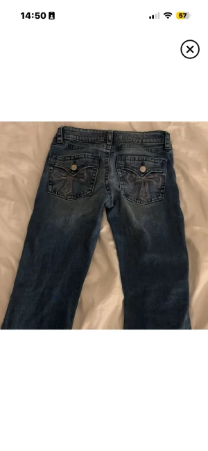 Blå jeans med broderade bakfickor - Snygga blå jeans med coola broderade detaljer på bakfickorna och silverfärgade knappar. Klassisk femficksmodell med rak passform och normal midja. Perfekta för dig som gillar jeans med lite extra stil.