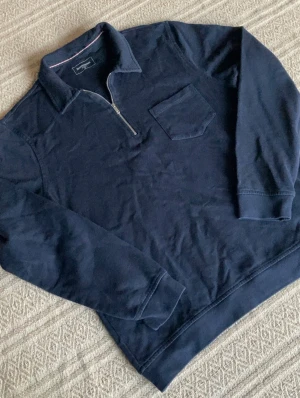 Half zip tröja Dressmann - Snygg marinblå långärmad tröja från Dressmann i storlek M. Tröjan har en klassisk krage, half zip-dragkedja och en bröstficka. Tillverkad i mjuk bomull som är skön mot huden. Perfekt för dig som gillar stilren och enkel design.
