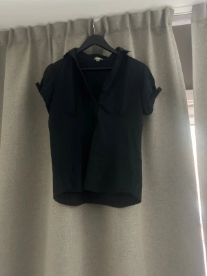 Svart kortärmad skjorta med krage - Svart skjorta med korta ärmar och klassisk krage. Skjortan har knappar framtill och en något lös passform. Perfekt för en stilren och enkel look.