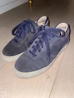 Mörkblå mockasneakers med snörning - Snygga mörkblå sneakers i mocka med klassisk vit sula och matchande mörkblå snören. Skorna har en rund tå och platt sula, vilket ger en clean och stilren look. Väl använda men inga slitningar, sula kan behöva bytas ut!