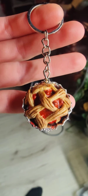 Nyckelring med pajdesign - Supergullig nyckelring som ser ut som en liten paj med flätat lock och röd fyllning. Pajen har detaljer i beige och rött och är fäst i en silvrig kedja med nyckelring. Perfekt accessoar för dig som älskar unika och roliga detaljer.