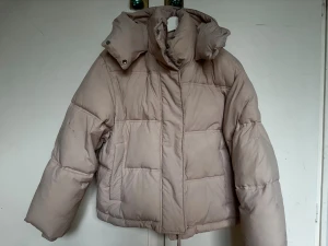 Ljusrosa pufferjacka med stor huva - Säljer en ljusrosa pufferjacka med oversized passform och stor, mysig huva från Mango. Jackan har dragkedja och tryckknappar framtill samt två stora fickor. Perfekt för kalla dagar och riktigt skön att bära. Fodrad och quiltad för extra värme. Har några små svarta fläckar på armarna (se bilder)