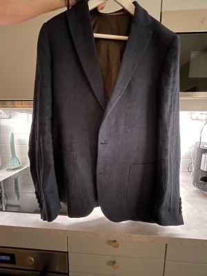 Mörkblå kavaj från Morris - Snygg mörkblå kavaj från Morris med klassisk passform. Kavajen har två knappar framtill, utanpåliggande fickor och knappar vid ärmsluten. Perfekt för dig som vill ha en stilren och tidlös look. I linne slim 