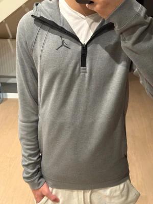 Jordan zip up - Snygg grå hoodie från Jordan med half zip och huva. Tröjan har lång ärm, svart Jordan-logga på bröstet och praktiska fickor med dragkedja. Perfekt för dig som gillar sportig och clean stil. Materialet är mjukt och känns skönt mot huden. Köpt för ca ≈1099